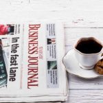Porcelain cup with coffee and newspapers on table