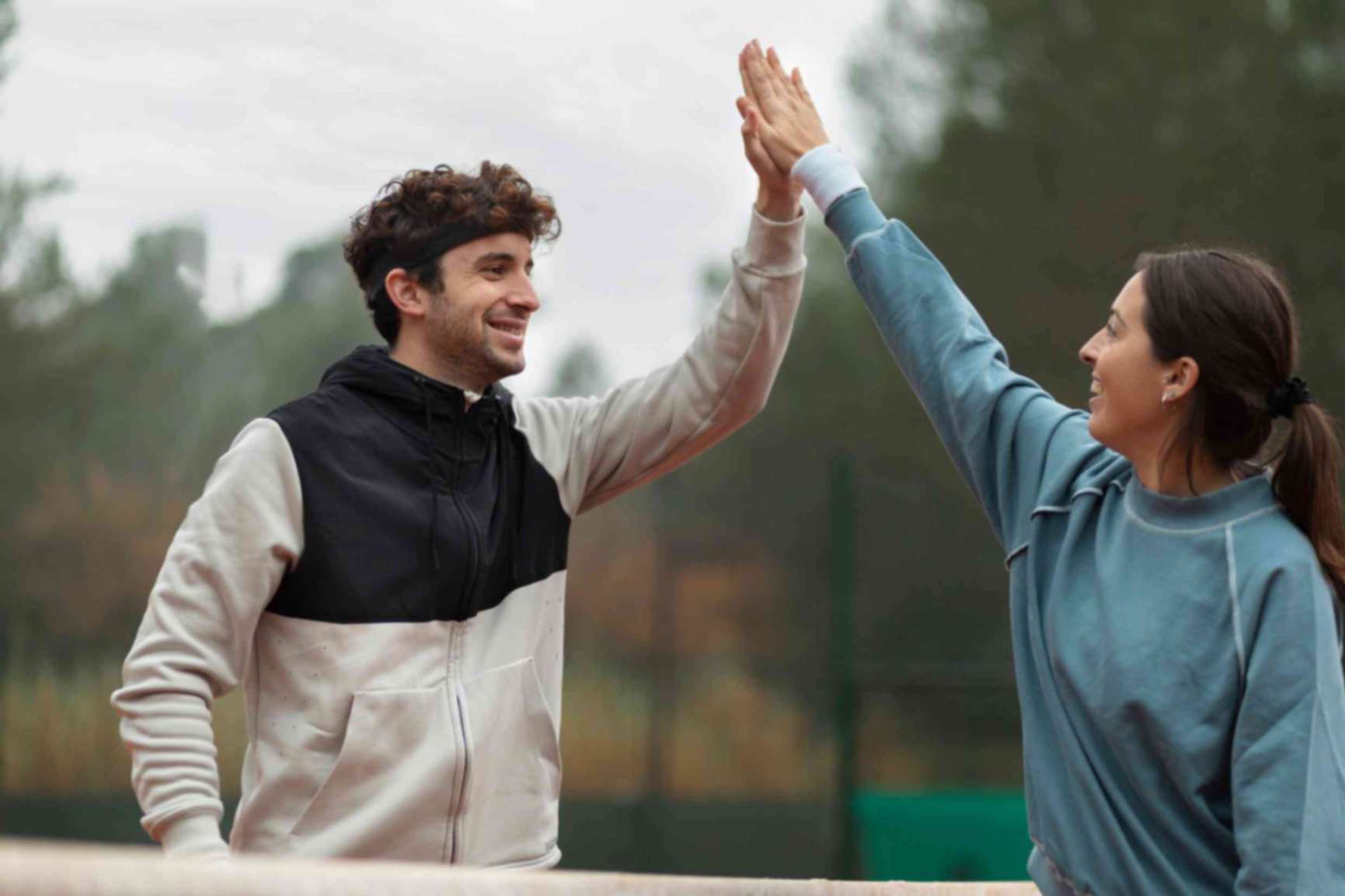 A man and woman doing high five standing in a tennis court 