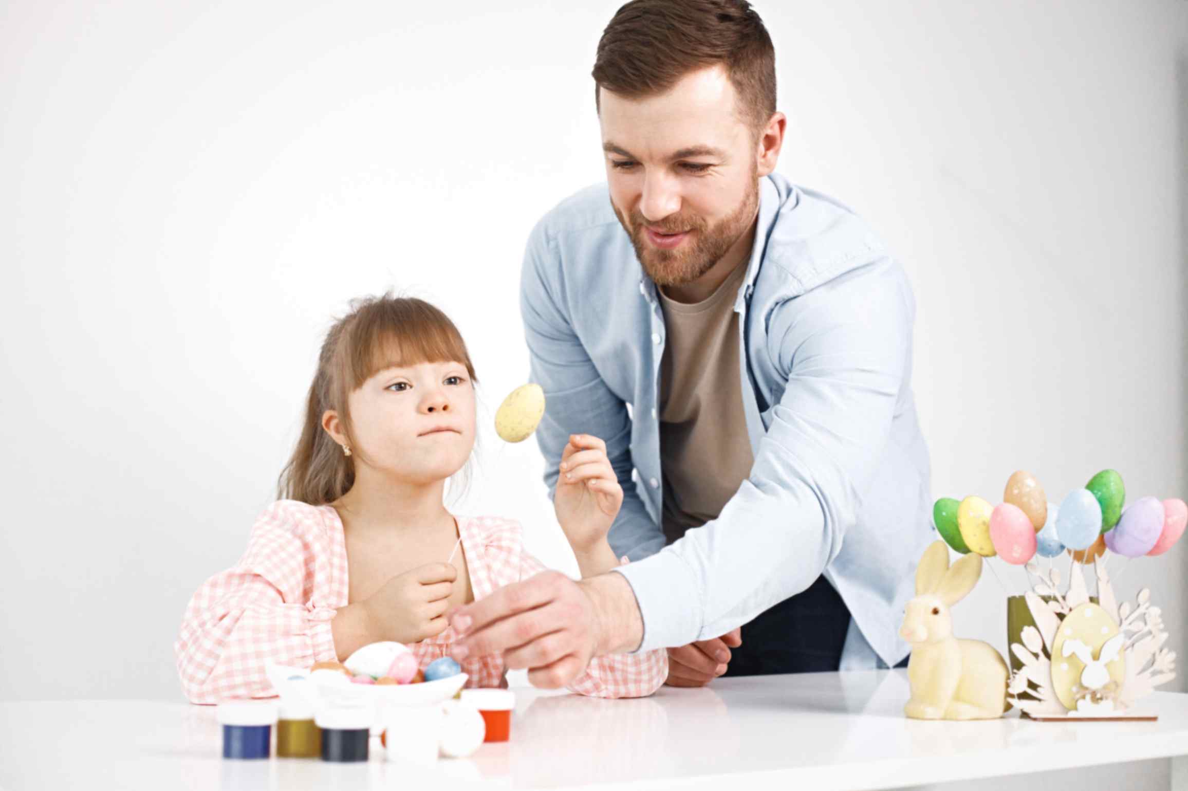 Girl with down-syndrome and her father playing with easter-colored eggs