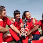 Girls celebrating their win in sports holding-cup and wearing medals