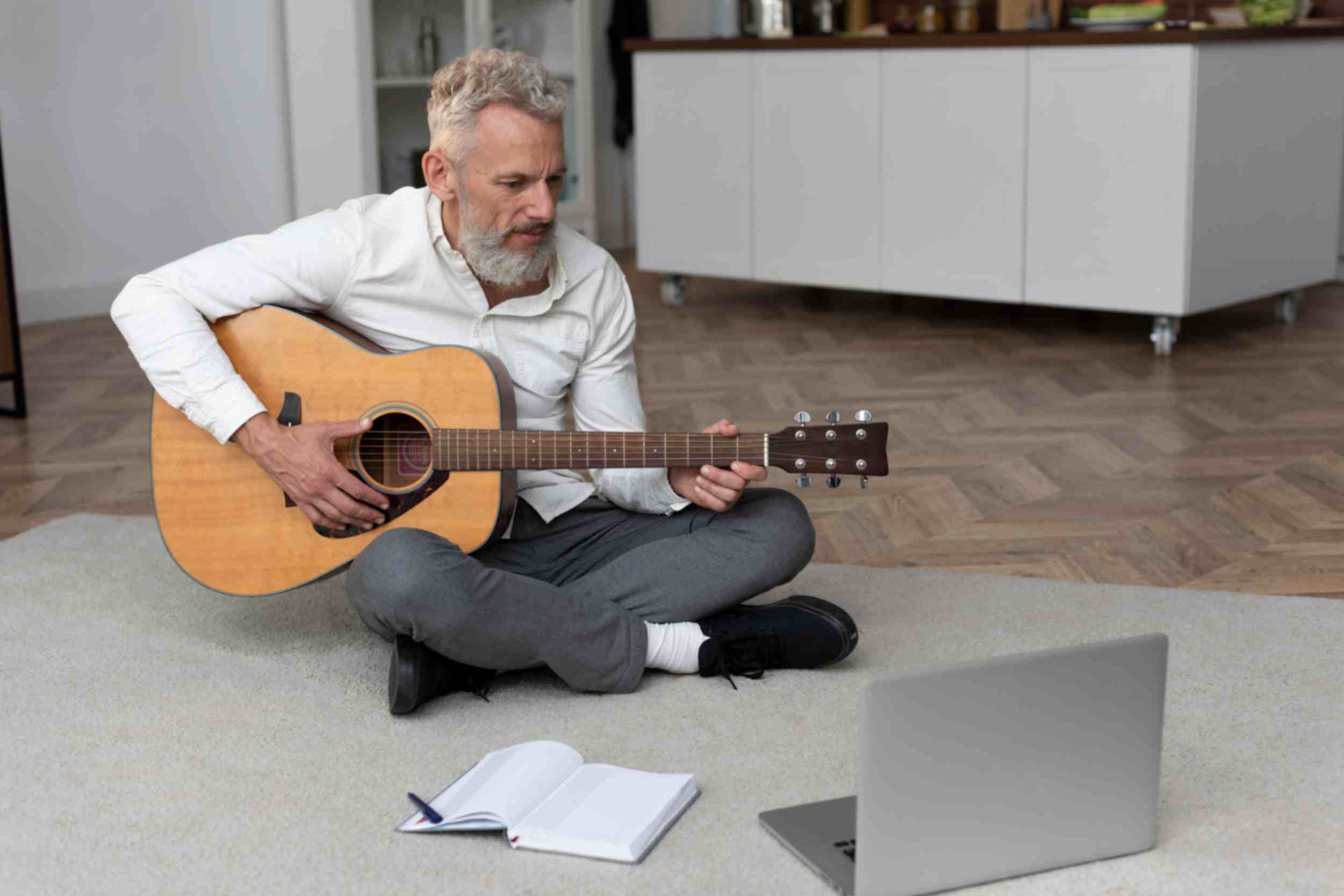 Senior man sitting o home floor taking guitar lessons