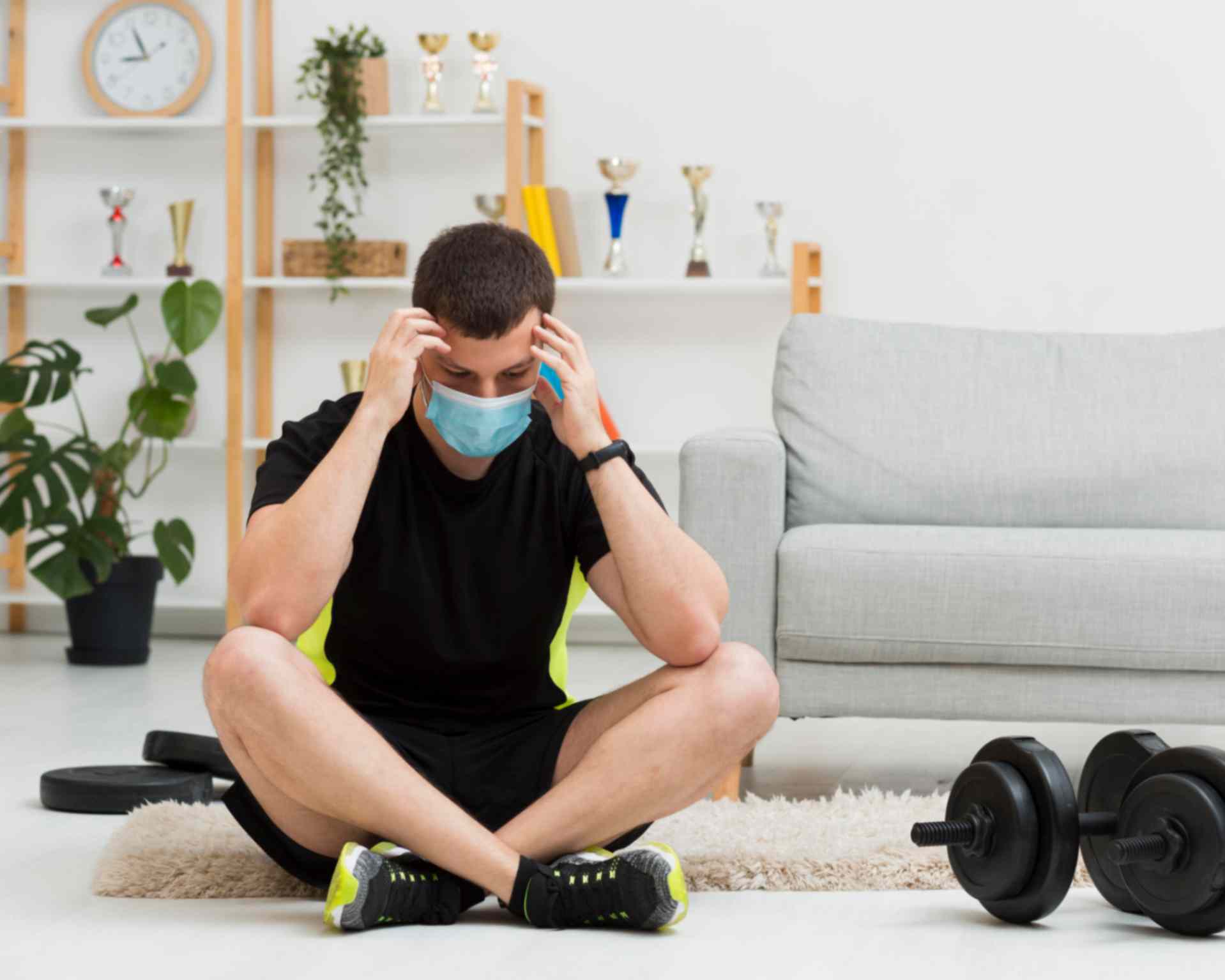 Man wearing gym wear and medical mask sitting next to gym equipment