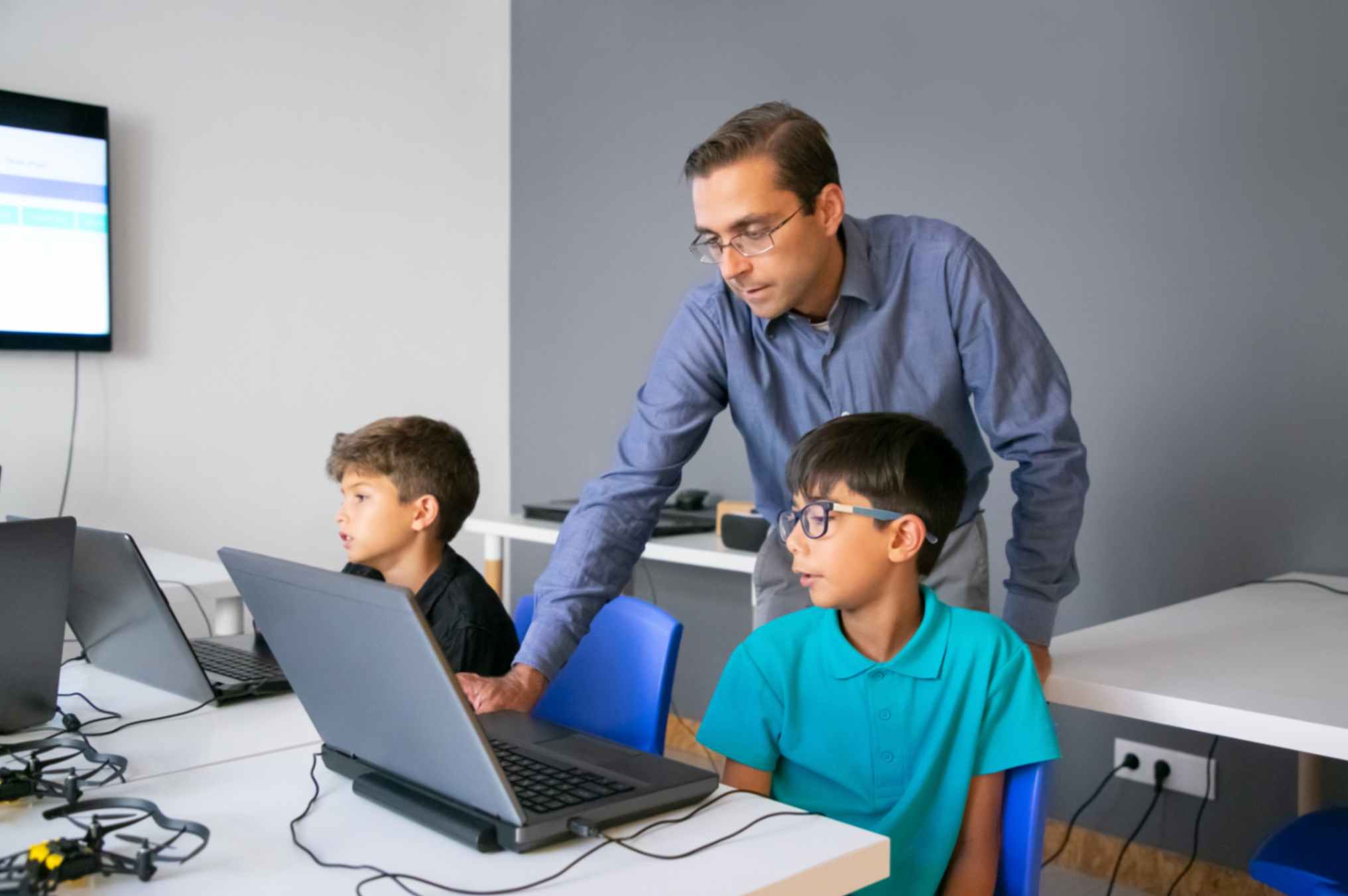 Teacher standing behind pupil teaching them how to use laptop.