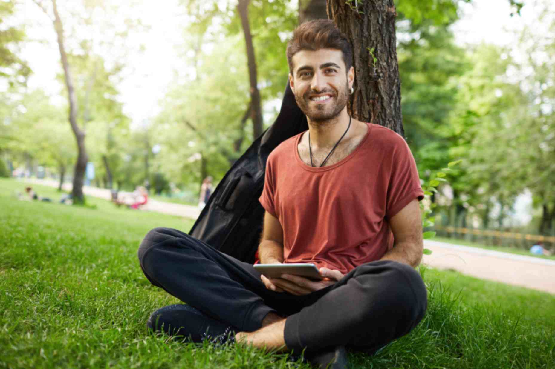 handsome guy sitting in park reading e book on digital tablet